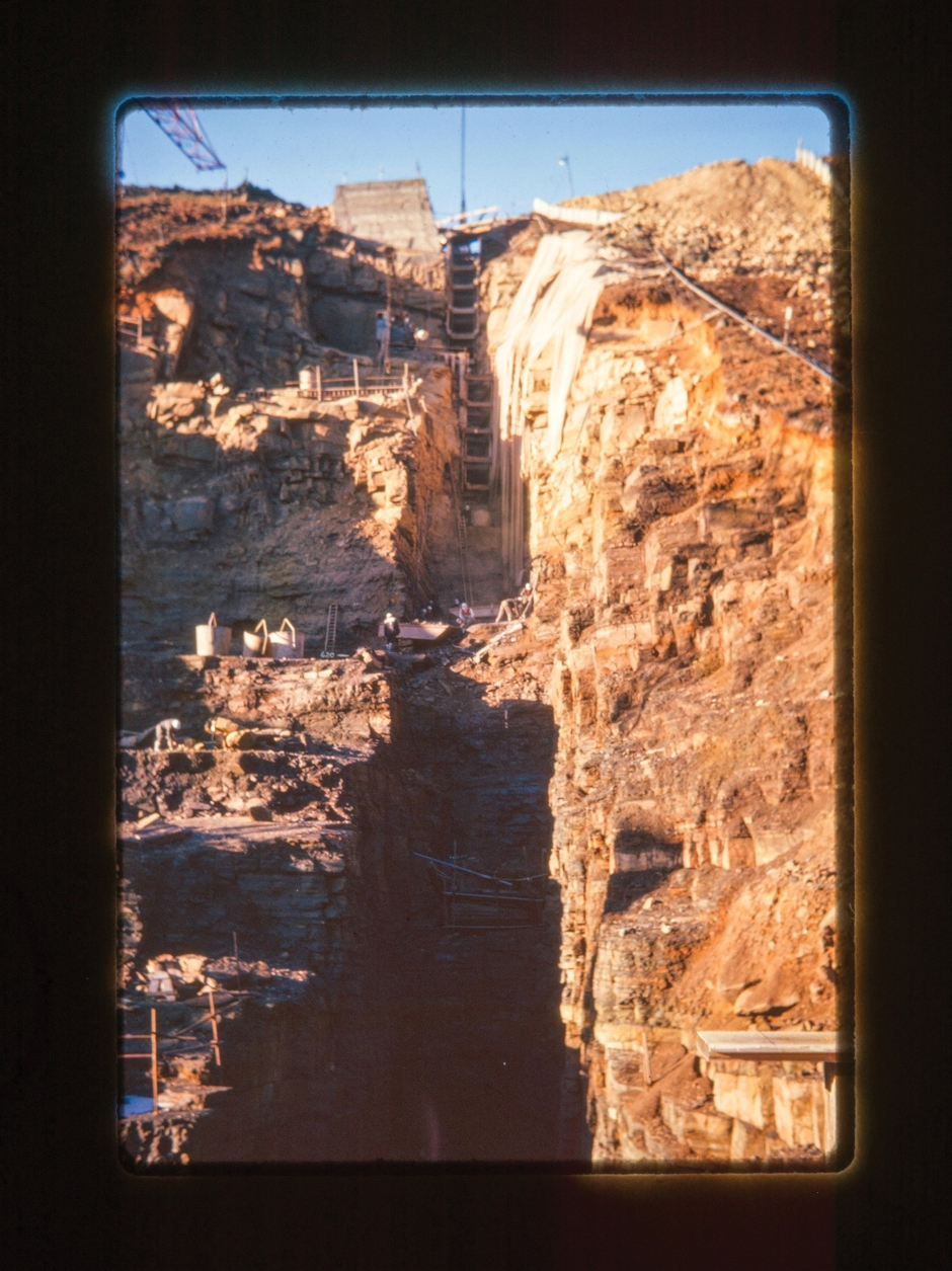 A cross-­section of the eastward dam shows the scale and size of the dam wall. Workers in the ­middle of the image look minute compared to the vast cavity that has been dug into the side of the valley.