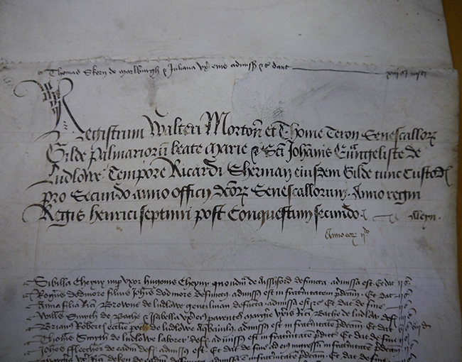 Two pieces of parchment are sewn together with visible stitching. An introductory paragraph is provided near the top of the second piece of parchment, stating that the document records the names of brothers and sisters of the Palmers’ Guild during the wardenship of Richard Sherman. A list of names, with relating occupations and locations, follow.