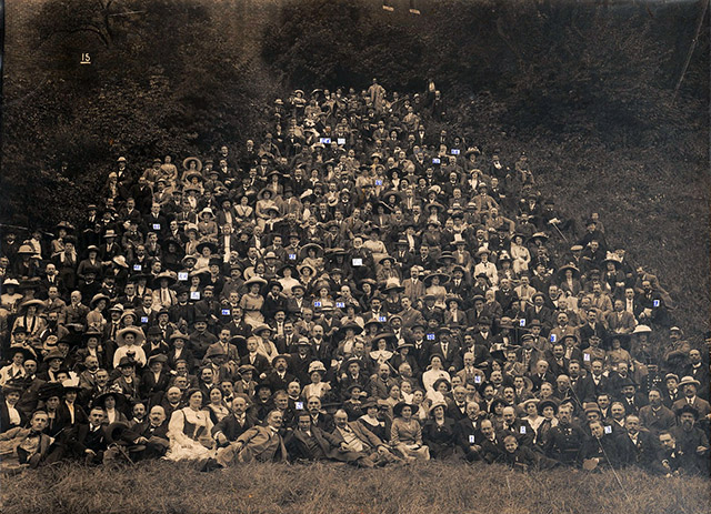 A black-and-white group photograph where over 200 participants of the Eight Universal Congress of Esperanto, in Kraków, 1912, appear together. The photograph includes men, women and children, all wearing formal attires such as suits, long dresses and hats. They all sit or lie down in the Wawel Slope, a hillside where Wawel Castle in situated, in Kraków.